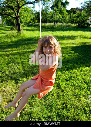 '4 year old' German Girl in orange dress playing on an outdoor swing with a green pasture behind her.. Model released Stock Photo