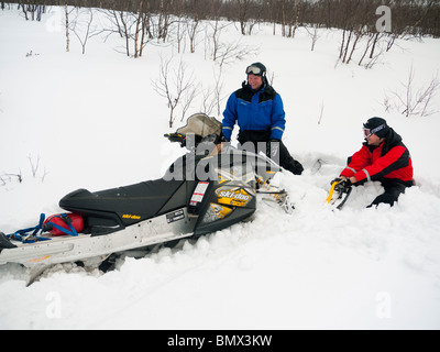 Two men, 25 and 45 years old, pull a deadlocked snow mobile out of the deep snow. Stock Photo