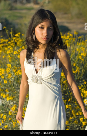 https://l450v.alamy.com/450v/bmx9ed/a-young-and-very-pretty-mixed-race-woman-is-wearing-a-white-formal-dress-with-a-patch-of-yellow-flowers-in-the-background-bmx9ed.jpg