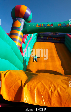 Young boy sliding down a brightly coloured inflatable slide at a funfair Stock Photo