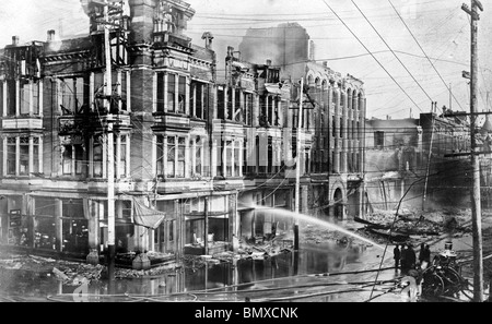 Block of burned buildings in San Francisco after the 1906 earthquake with fire truck spraying water on them. June 1906 Stock Photo