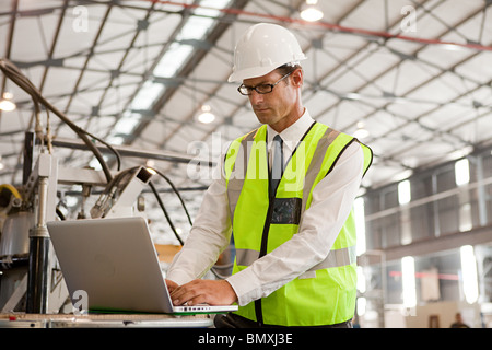 Mature man using laptop in factory Stock Photo