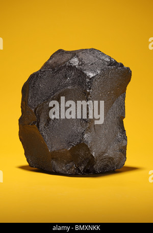 A large piece of black bituminous coal on a bright yellow background Stock Photo