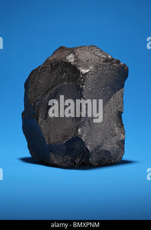 A large piece of black bituminous coal on a bright blue background Stock Photo