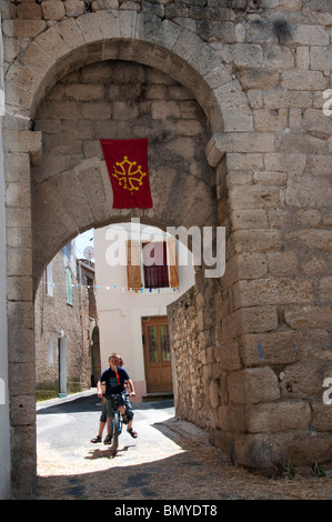 Two boys on a bicycle ride through a mediaeval gateway in the small southern French town of St Genies de Fontedit Stock Photo