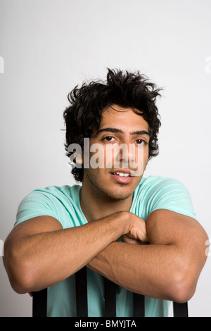 Portrait of Young dark haired guy with arms folded over chair Stock Photo