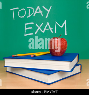 Today exam written on a chalkboard. Books, pencils and an apple on foreground. Stock Photo