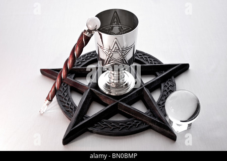 An altar ritual set up on a white background, using a Pentacle, Gemstone Quartz Chalice, Wand and Crystal Ball. Stock Photo