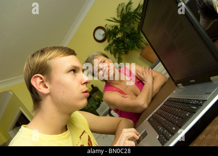 Young boy who has mild autism at home working on laptop with mum in background, Sutton, UK. Model released (MR). Stock Photo