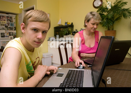 Young boy who has mild autism at home with his mum working on laptop, Sutton, UK. MR Stock Photo
