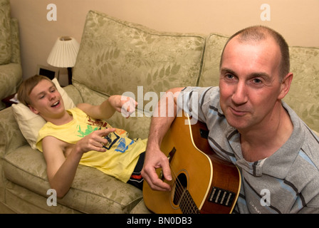 Young boy who has mild autism at home with his dad playing guitar, Sutton, UK. Stock Photo