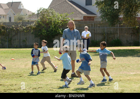 Male student teacher supervises while students play during recess at Great Oaks Elementary School in Round Rock, Texas, USA. Stock Photo