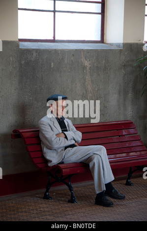 An old man with his arms and feet crossed sat on a bench in Funchal, Madeira. Stock Photo