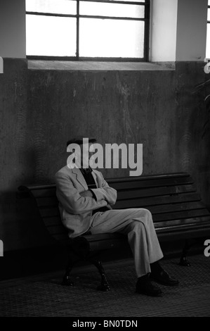 An old man with his arms and feet crossed sat on a bench in Funchal, Madeira. (Black and White) Stock Photo