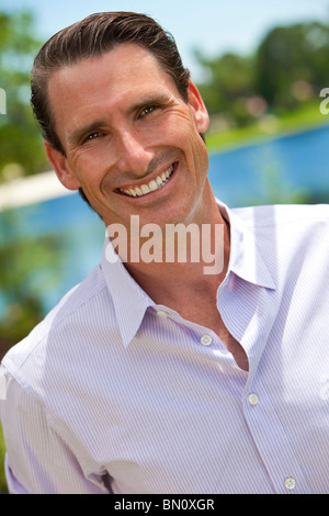 An outdoor portrait of smiling handsome middle aged man shot with sunlight against a natural background with a lake Stock Photo