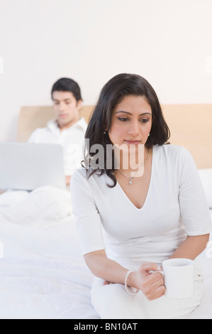 Woman drinking tea with a man working on a laptop in the background Stock Photo