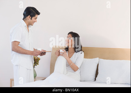 Man giving tea to a woman on the bed Stock Photo