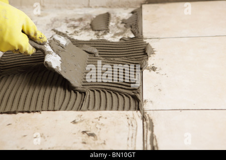 Tiler installing ceramic tiles on a floor using notched trowel Stock Photo