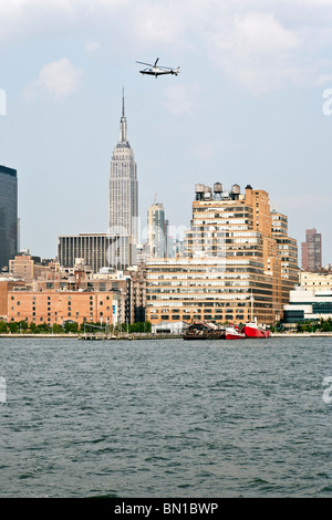 low flying helicopter above Hudson river against water view Manhattan skyline including Empire State & Starrett Lehigh building Stock Photo