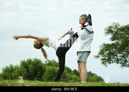 Mature couple stretching in park, man holding woman's leg as she does backwards bend Stock Photo