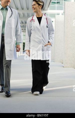 Female doctor walking with colleague along hospital corridor Stock Photo