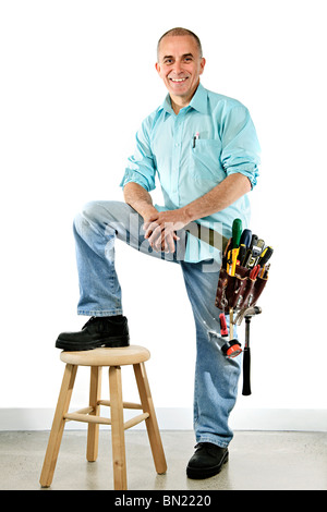 Portrait of smiling handyman with tool belt and stool Stock Photo