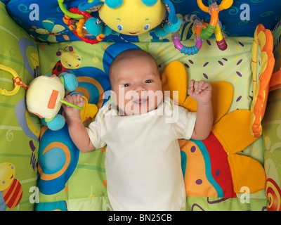 Happy smiling six week old cute baby boy lying in a colorful play mat with toys Stock Photo