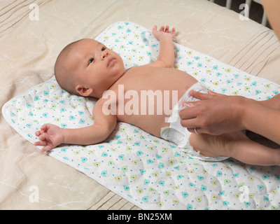 Six week old cute baby boy lying on a bed while mother is changing his diaper Stock Photo