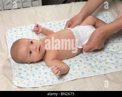 Six week old cute baby boy lying on a bed while mother is changing his diaper Stock Photo