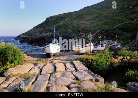 Fishing boats lined up on a stone beach slipway in a quiet Cornish cove Stock Photo