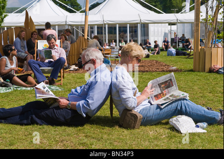 Mature couple reading newspapers sitting back to back on grass in the sunshine at Hay Festival 2010 Hay on Wye Powys Wales UK Stock Photo