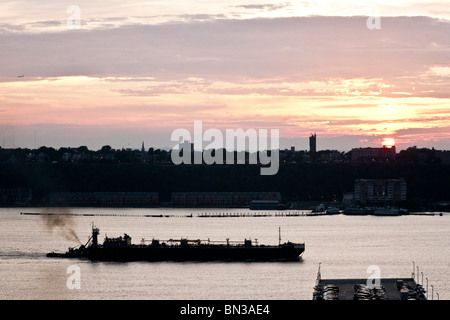 river view from West Side Manhattan of tug pushing barge up Hudson river as sun sets over New Jersey Palisades Stock Photo