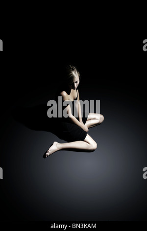 Young woman in black dress sitting on floor Stock Photo