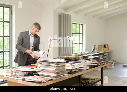 Man standing in front of a table with magazines and books and reading a book Stock Photo