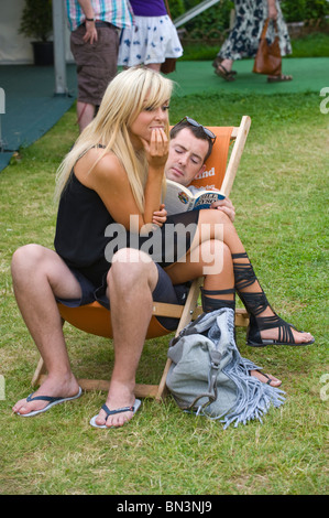 Young man reading book sitting in deckchair with young blonde woman sat on his lap at Hay Festival 2010 Hay on Wye Powys Wales Stock Photo