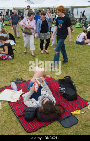 Young woman reading book lying on travel rug amongst crowd at Hay Festival 2010 Hay on Wye Powys Wales UK Stock Photo