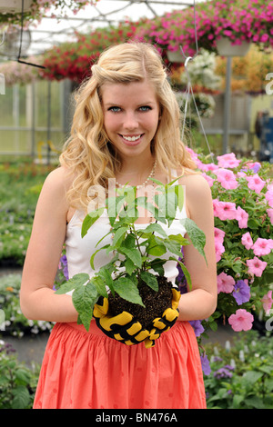 Beautiful young woman holding plant inside green house Stock Photo