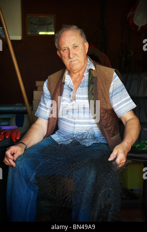 grey haired elderly farmer sits in his shed while holding netting ready for planting in allotment Stock Photo