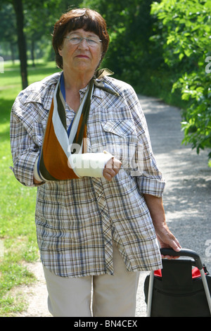 Senior woman takes a walk in the park with cast arm in sling and broken arm Stock Photo