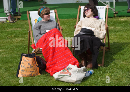 Two young women sitting in deckchairs chatting in the summer sunshine at Hay Festival 2010 Hay on Wye Powys Wales UK Stock Photo