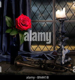 rose on a window seal lite by a candle with an old trumpet with dark sky Stock Photo