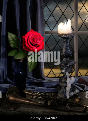 rose on a window seal lite by a candle with an old trumpet and dark sky Stock Photo