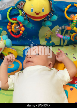 Six week old cute baby boy lying in a colorful play mat with toys Stock Photo