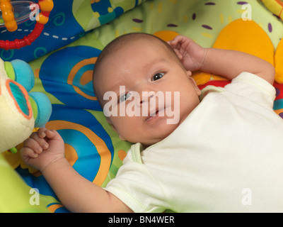 Six week old cute baby boy lying in a colorful play mat with toys Stock Photo