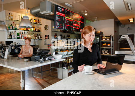 Woman drinking coffee in coffee shop, whilst working on her laptop computer. Stock Photo