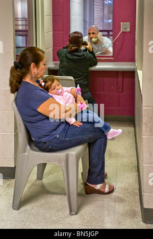 Prisoner talks with his wife on a telephone at the Santa Ana, CA,  jail.  His mother-in-law cares for their baby. MODEL RELEASE Stock Photo
