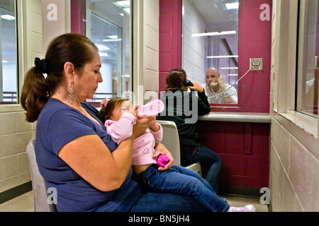 Prisoner talks with his wife on a telephone at the Santa Ana, CA,  jail.  His mother-in-law cares for their baby. MODEL RELEASE Stock Photo