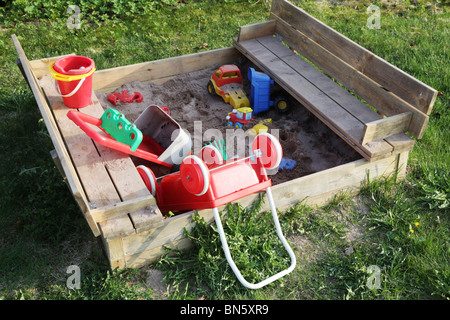 A sandpit in a garden filled with abandoned plastic toys Stock Photo
