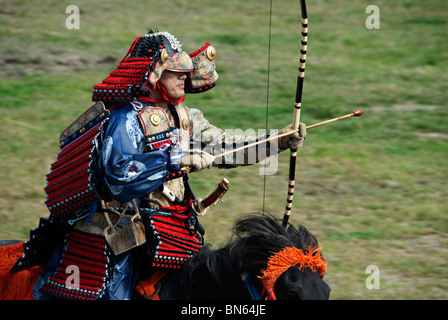 A Japanese man, dressed in traditional armor, prepares to shoot an arrow during a Yabusame (mounted archery) contest. Stock Photo