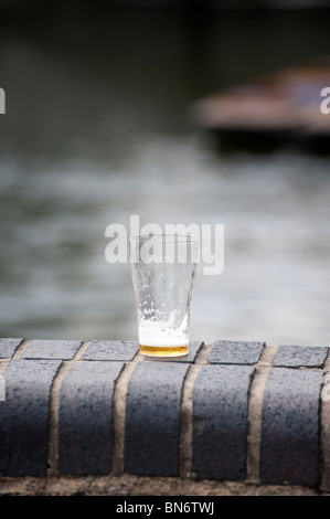 Almost empty pint glass of beer on wall at the Millpond Cambridge showing out of focus punts in background on sunny summer  day. Stock Photo